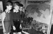 An exhibit at a Berlin school persuades Germans to help colonize the Warthegau area of Poland. The exhibit says “The land calls you!,” and the painting shows a settler’s car passing by a Polish border sign that has been knocked down.