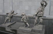 A statue featuring a woman running, holding hands with a young girl while another young girl trails behind them. All show expressions of fear and distress on their faces.