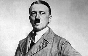 Portrait of Adolf Hitler in a brown trenchcoat, shirt, and tie.