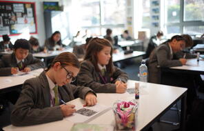 Uniformed middle school students complete assignments at their desks. 