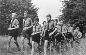 A group of boys in Hitler Youth uniforms walk through a field