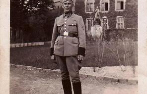 A full body photographic portrait of a middle-aged man in uniform in front of a mansion