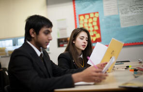 Uniformed high school students read at their desks. 