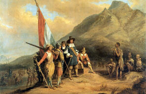 Group of 17th century European explorers carrying supplies and a Dutch flag onto land, approached by indigenous people.