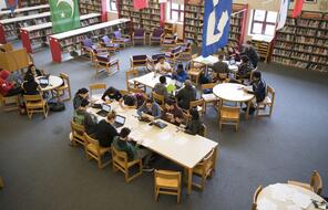 A bird’s eye view of students sitting at tables in a library.