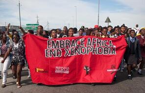 Group of black South African protestors carrying a red banner that says "EMBRACE AFRICA. END XENOPHOBIA"