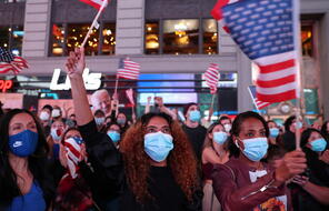 Masked crowd holding American flags celebrate as they hear that Joe Biden won the 2020 US Presidential election.