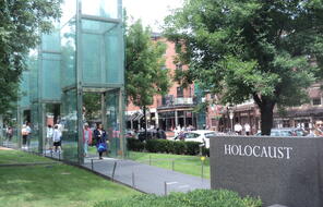 A stone sign on the right reads Holocaust, with three glass pillars in view at the New England Holocaust Memorial in Boston, MA.