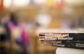 Two Holocaust and Human Behavior books are stacked on a table and the background is blurred out.