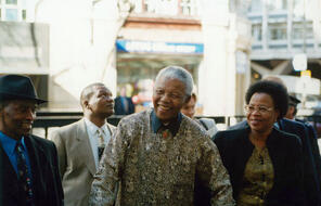 Nelson Mandela standing outdoors during daytime surrounded by 4 other people. 