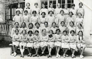 A group of Tunisian schoolgirls in aprons pose in four rows.