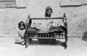 Armenian woman with baby in cradle, another child sits beside her
