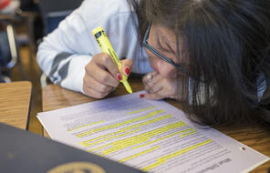 A student highlights a paper at their desk.