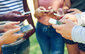 Cropped shot of a group of friends using their phones together outdoors
