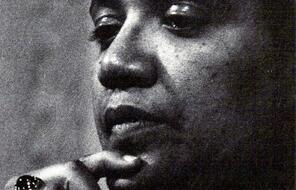 A headshot of Audre Lorde taken in 1980; her finger rests on her chin, and she is looking down