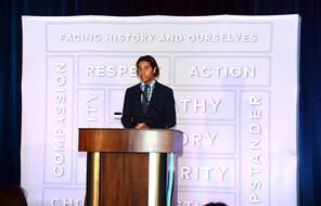 A Facing History student stands at a podium giving a speech at a Facing History benefit dinner.