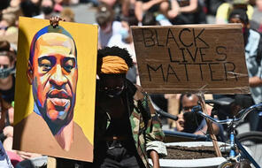 A protester holding a painting of George Floyd and a sign that reads "Black Lives Matter"