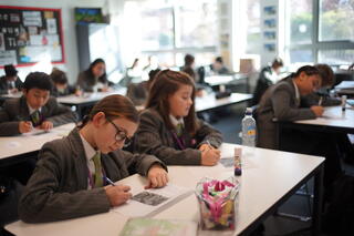 Uniformed middle school students complete assignments at their desks. 