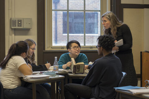 A teacher hands out papers to students at a table. 