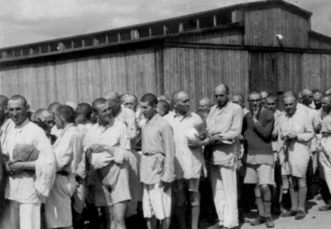 Men in prison uniform and shaved heads stand in line.