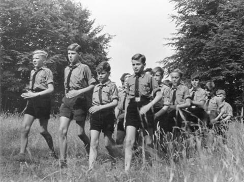 A group of boys in Hitler Youth uniforms walk through a field