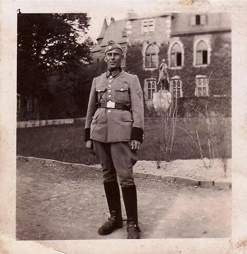 A full body photographic portrait of a middle-aged man in uniform in front of a mansion