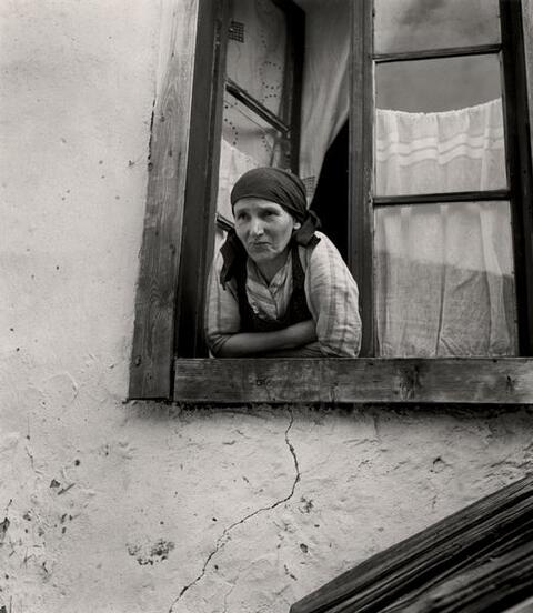 A woman wearing a scarf on her head leans out of a window. Photo taken circa 1935-1938.