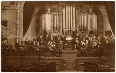 A full orchestra on stage with a pipe organ in the background, circa 1930s.