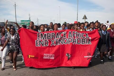 Group of black South African protestors carrying a red banner that says "EMBRACE AFRICA. END XENOPHOBIA"