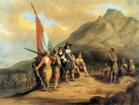 Group of 17th century European explorers carrying supplies and a Dutch flag onto land, approached by indigenous people.