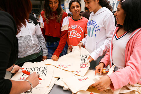 Five students stand around a table writing on canvas bags which read, "Knock Down [blank]."