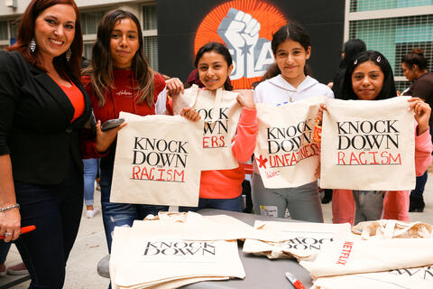 Four students and one teacher pose for a picture holding canvas bags which read "Knock Down the Racism."