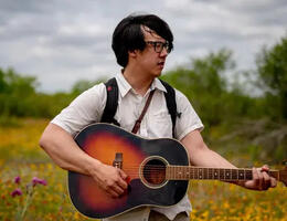 Picture of Julian Saporiti of No-No Boy playing the guitar in a field.