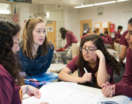 A teacher talking with three high school students in a classroom