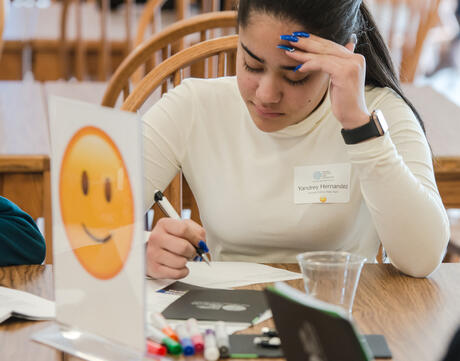 A student looks down at their paper with a pen in hand. A smiling emoji is in the foreground.