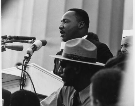 Dr. Martin Luther King, Jr. stands at a microphone giving a speech to a crowd.
