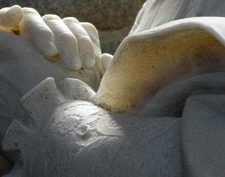 A close up of a marble statue with hands clasped together.
