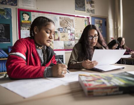 Two female students work together at their desks.