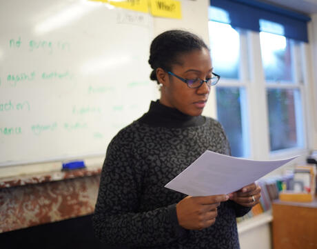 Woman educator of color reads to the classroom.