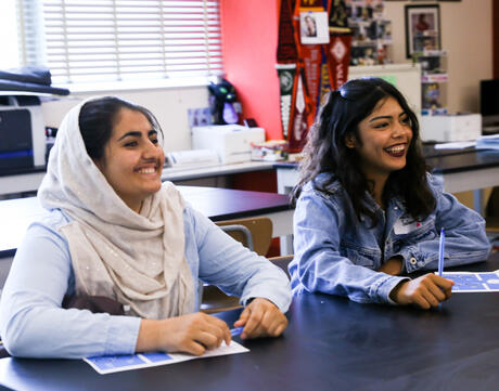 Two female students, one with a hijab, sit in classroom.