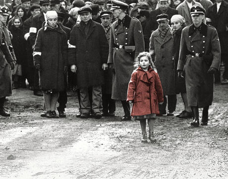 Picture of a little girl in a red coat standing in front of people.