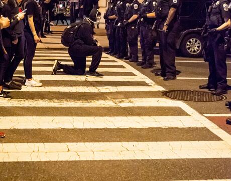 Demonstrators peacefully protest in front of police officers during a Black Lives Matter protest. One protester takes a knee in front of the officers.