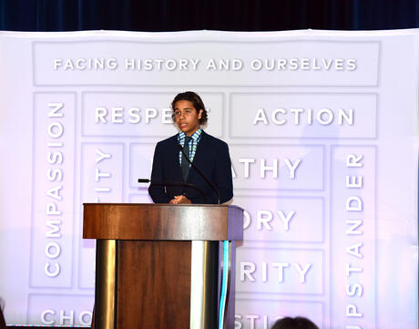 A Facing History student stands at a podium giving a speech at a Facing History benefit dinner.