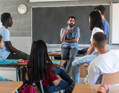 Young teacher talking with teenager students sitting at school classroom